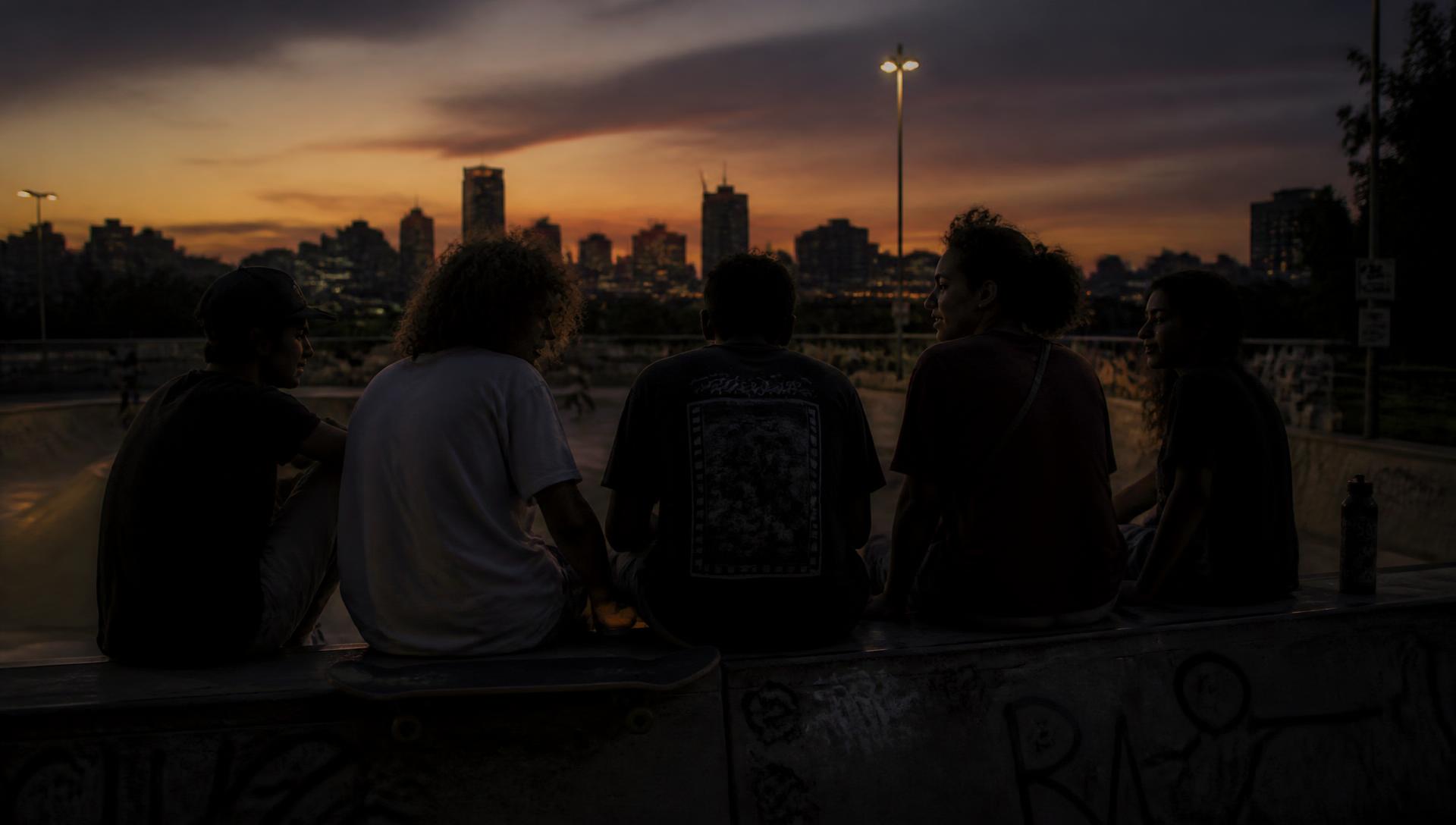 Skaters sitting on the edge of a skatepark bowl at dusk